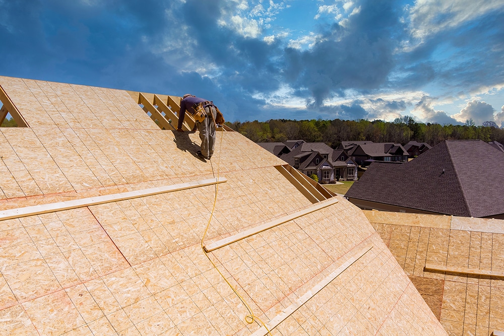 Workers applying nailing plywood panels a roof on the new house